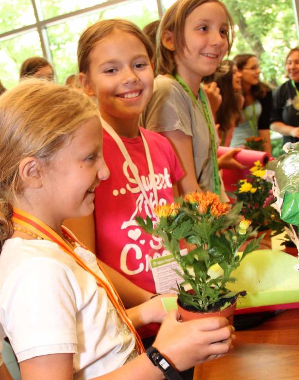 Mehrere Kinder stehen an einem Tisch mit kleinen Topfpflanzen.