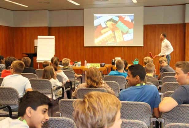 Kinder sitzen in einem Raum und schauen auf eine Projektion von Legosteinen.