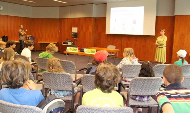 Kinder sitzen in einem Raum und hören einem Vortrag zu.