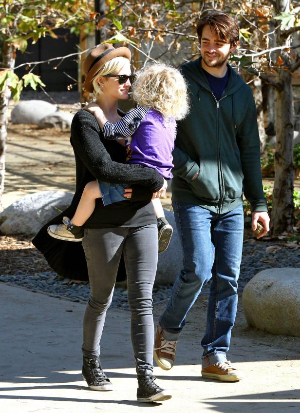 Eine Frau mit Hut trägt ein Kind, während ein Mann daneben geht.