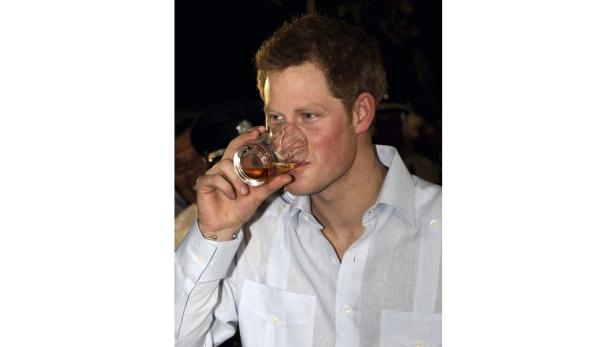 Prinz Harry trinkt aus einem Glas mit bernsteinfarbener Flüssigkeit.