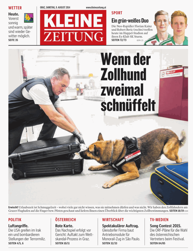 Ein Zollhund schnüffelt an einem Gepäckstück, während ein Beamter daneben steht.
