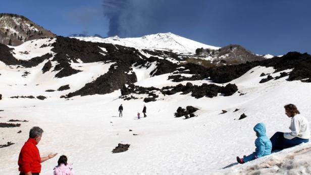 Eine Gruppe von Menschen genießt einen sonnigen Tag im Schnee am Hang eines Vulkans.
