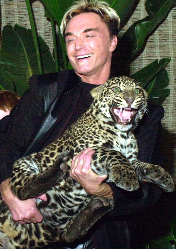 Ein Mann hält einen jungen Leoparden im Arm und lächelt.