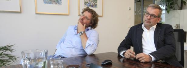 Zwei Männer sitzen an einem Tisch in einem Büro.