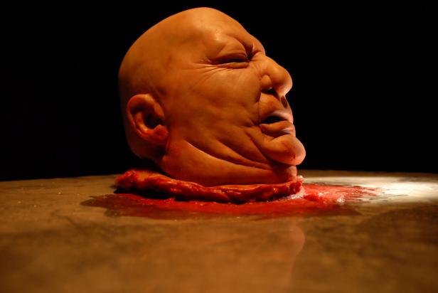 Ein abgetrennter Kopf liegt auf einem Tisch, umgeben von Blut.