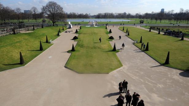 Blick über einen formellen Garten mit Rasenflächen, Wegen und kegelförmigen Bäumen.