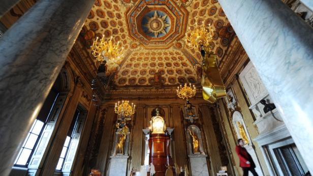 Innenansicht eines prunkvollen Saals mit Marmorsäulen, goldenen Statuen und einem verzierten Deckengemälde.