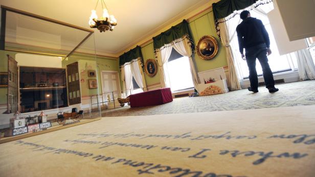 Ein Puppenhaus und ein Mann stehen in einem Raum mit historischen Möbeln.