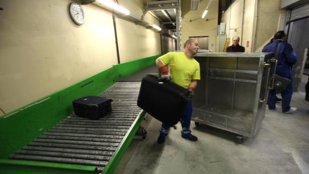 Ein Gepäckarbeiter hebt einen schweren Koffer in einem Lagerraum.