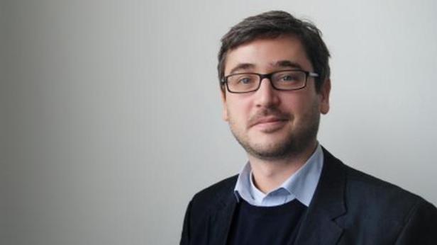 Ein Mann mit Brille und dunklem Sakko lächelt in die Kamera.