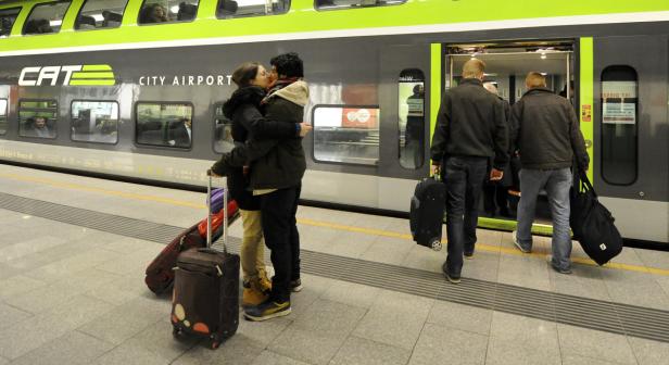 Ein Paar umarmt sich vor einem CAT City Airport Zug am Bahnsteig.