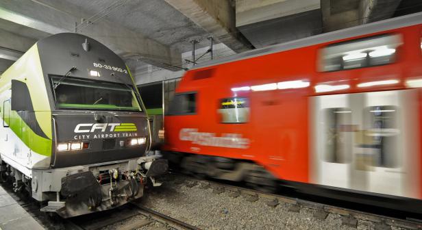 Ein CAT City Airport Train steht neben einem vorbeifahrenden Cityshuttle-Zug.