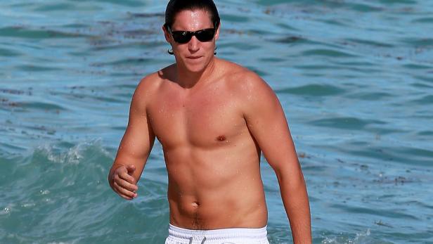 Ein Mann mit Sonnenbrille geht im Meer entlang.