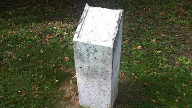 Ein schlichter, grauer Grenzstein steht auf einer Wiese.