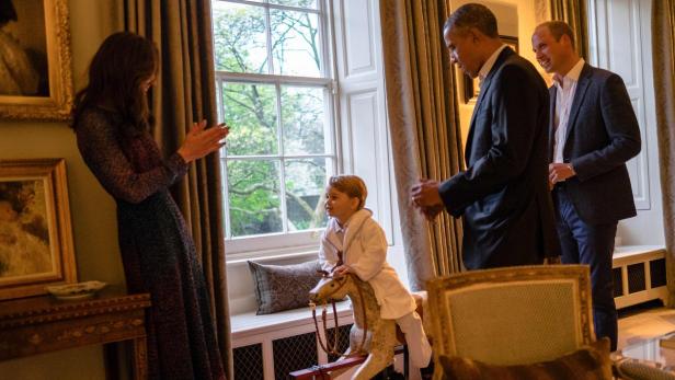 Prinz George auf einem Schaukelpferd mit Kate Middleton, Barack Obama und Prinz William im Hintergrund.