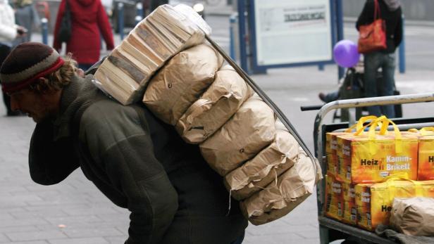 Ein Mann trägt einen schweren Stapel Brennholz und Briketts auf dem Rücken.