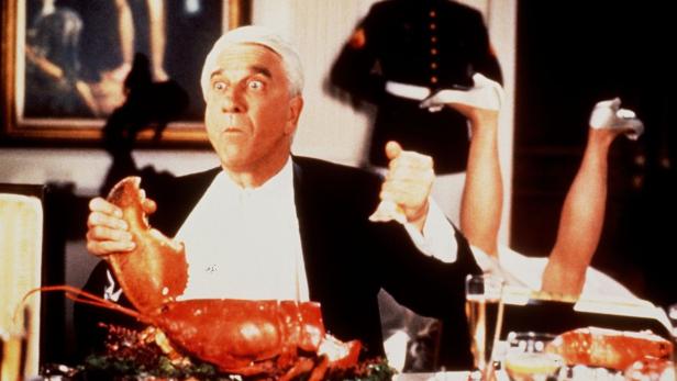 Leslie Nielsen mit einem Hummer bei einer komischen Szene, möglicherweise aus „Die nackte Kanone“.