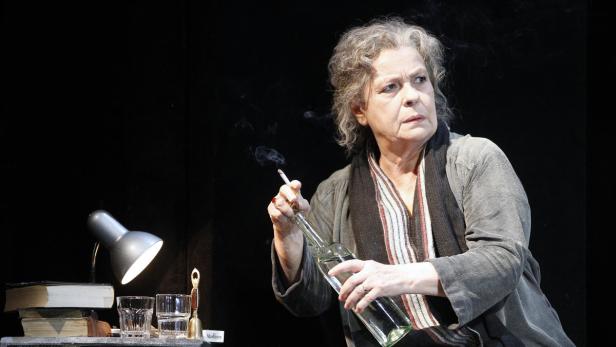 Eine ältere Frau hält eine Zigarette und eine Flasche in der Hand.