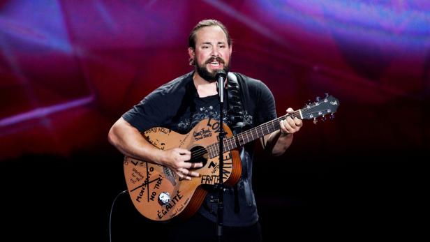 Ein bärtiger Mann singt und spielt Gitarre mit politischen Botschaften auf der Bühne.