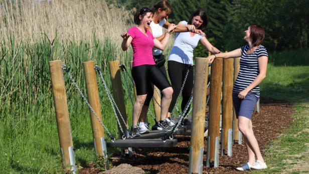 Vier Frauen überqueren lachend einen wackeligen Steg in einem Park.