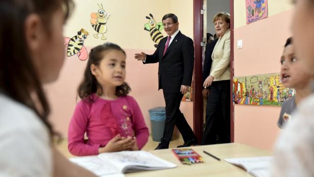Angela Merkel und ein Mann im Anzug besuchen eine Schulklasse.