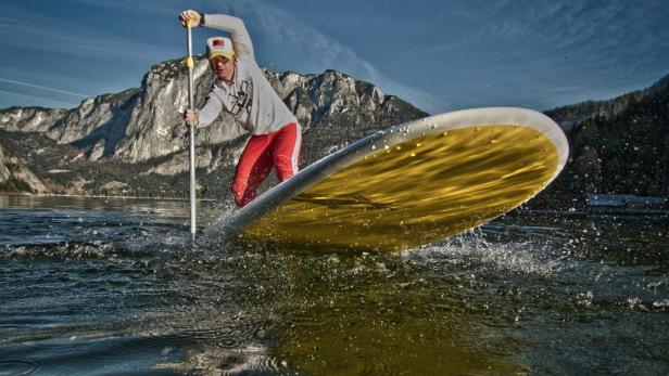 Ein Mann paddelt auf einem gelben Stand-Up-Paddleboard auf einem See.
