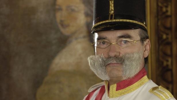 Ein Mann in historischer Uniform mit markantem Backenbart und goldenen Brillengläsern.