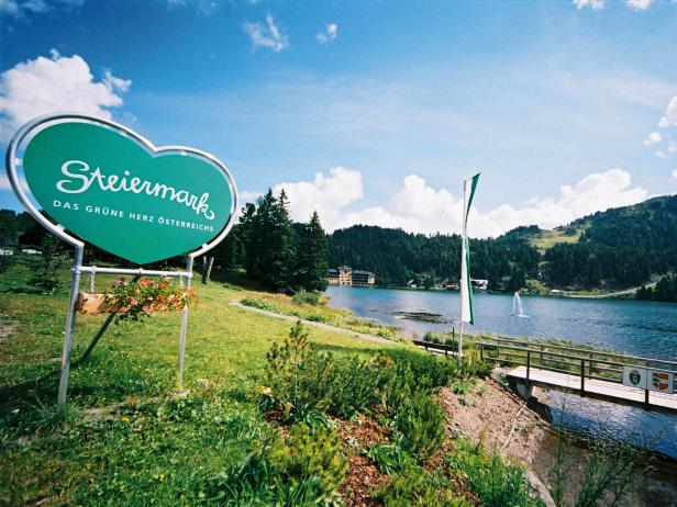Ein Schild mit der Aufschrift „Steiermark – Das grüne Herz Österreichs“ vor einem Bergsee.