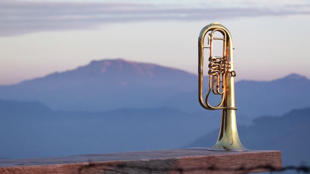 Ein Flügelhorn steht auf einem Holzbalken vor einer Bergkulisse.