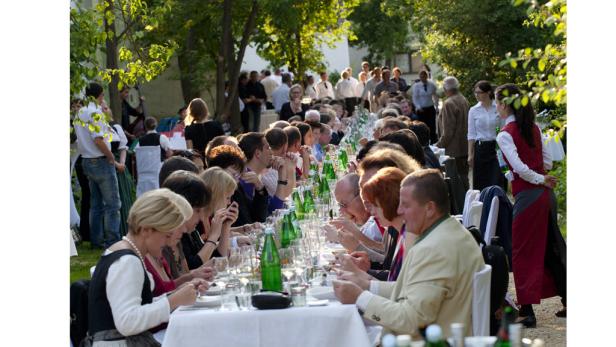 Eine lange Tafel ist im Freien für eine große Gruppe von Menschen gedeckt.