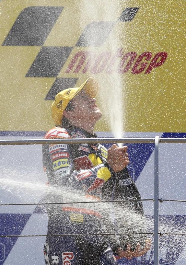 Ein Motorradrennfahrer feiert seinen Sieg mit einer Champagnerdusche vor dem MotoGP-Logo.