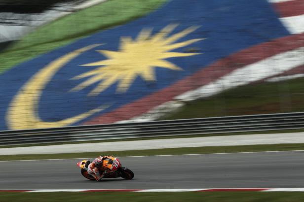 Ein Motorradfahrer rast auf einer Rennstrecke vor einer großen Flagge Malaysias.