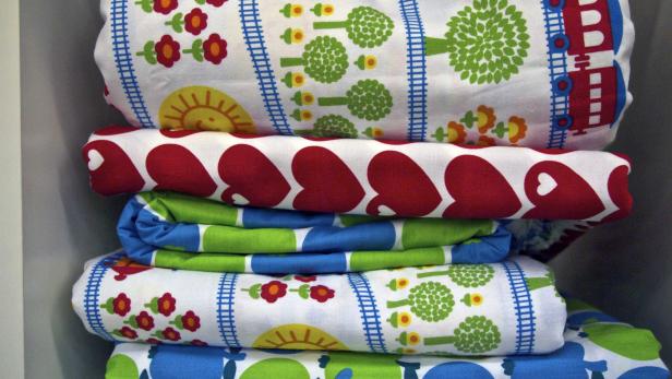 Ein Stapel bunter Stoffe mit Mustern wie Herzen, Blumen, Bäumen und Zügen.