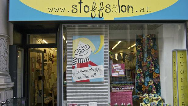 Die Fassade von „stoffsalon.at“ mit Schaufenster und einem Plakat mit der Aufschrift „Designerstoffe aus aller Welt“.