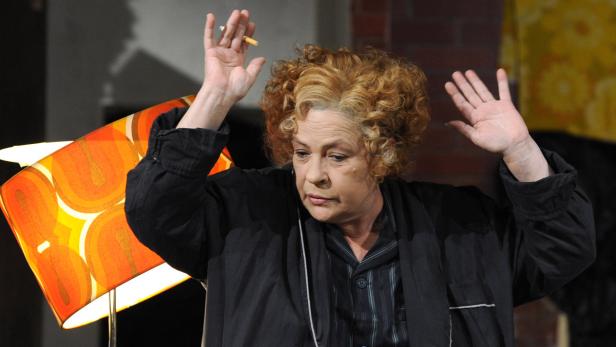 Eine Frau mit lockigem Haar gestikuliert mit einer Zigarette in der Hand.