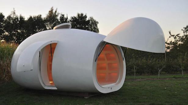 Ein weißes, eiförmiges Haus mit geöffneten Türen steht auf einer Wiese.