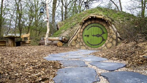 Ein grünes Hobbit-Haus mit runder Tür in einer bewaldeten Umgebung.