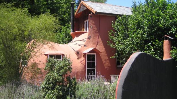 Ein Haus in Form eines Stiefels, umgeben von Bäumen und Büschen.