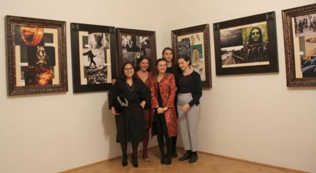Fünf Frauen posieren vor einer Wand mit gerahmten Kunstwerken in einer Galerie.