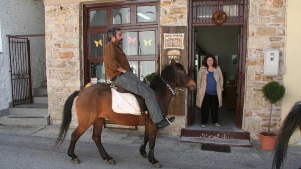 Ein Mann reitet auf einem Pferd vor einem Laden, während eine Frau in der Tür steht.