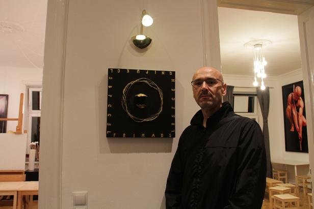 Ein Mann steht vor einem Wandbild mit goldenen Akzenten in einem Raum.