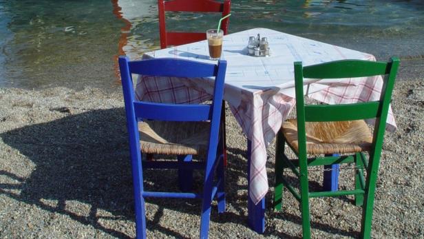 Ein Tisch mit Getränk und drei Stühlen steht am Strand.