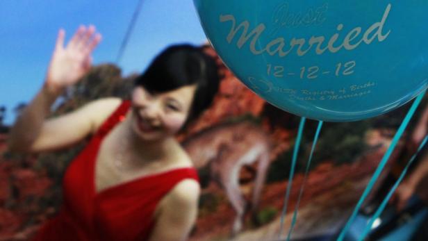 Eine Frau mit einem roten Kleid und einem „Just Married“-Ballon feiert ihre Hochzeit am 12.12.12.