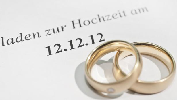 Zwei goldene Eheringe liegen auf einer Hochzeitseinladung mit dem Datum 12.12.12.