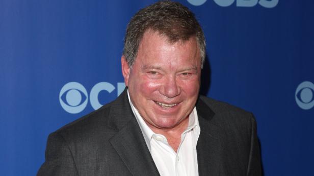 William Shatner lächelt vor einem blauen Hintergrund mit dem CBS-Logo.
