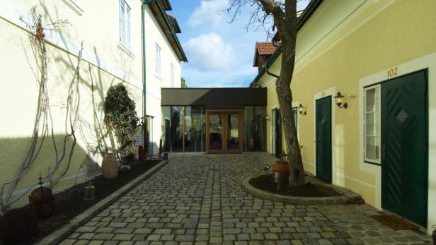 Ein gepflasterter Innenhof zwischen zwei gelben Gebäuden mit grünen Türen.