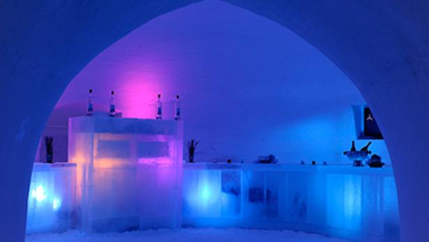 Eine Bar aus Eis mit Flaschen und Gläsern, beleuchtet in Blau und Violett.