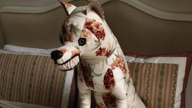 Ein Stofftier in Hundeform mit Blumenmuster steht auf einem Bett.