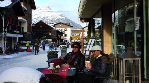 Ein Paar sitzt in einem Straßencafé in einem verschneiten Bergdorf.